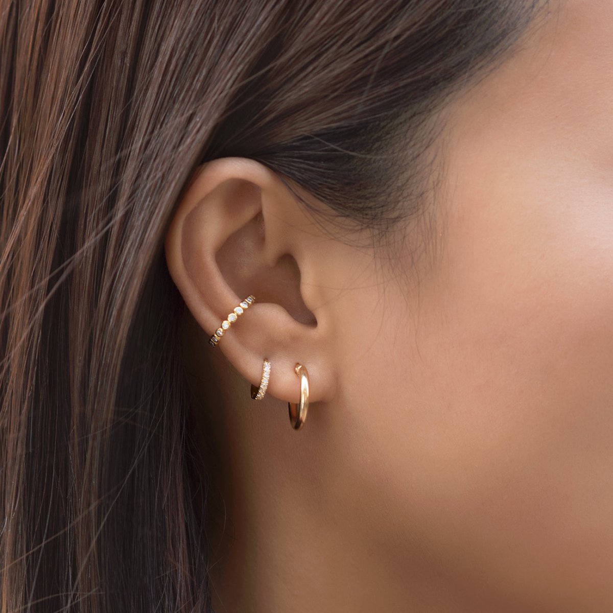 14K gold diamond pavé huggie hoop stacked with a plain hoop and ear cuffs on a model's ear