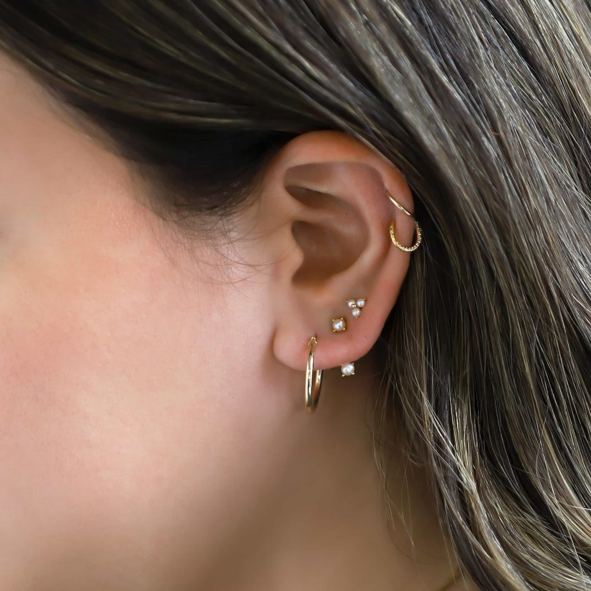 Gold titanium front pavé hoop with white zirconia, shown on a model's ear in a stack with pearl studs