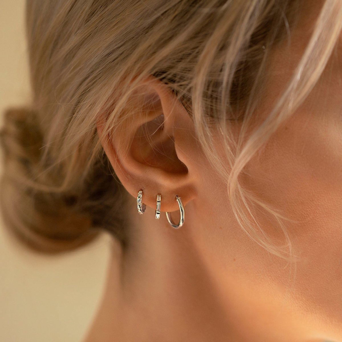 14K white gold pavé rope huggie hoops with clear stones, shown on a model's stacked ear lobe