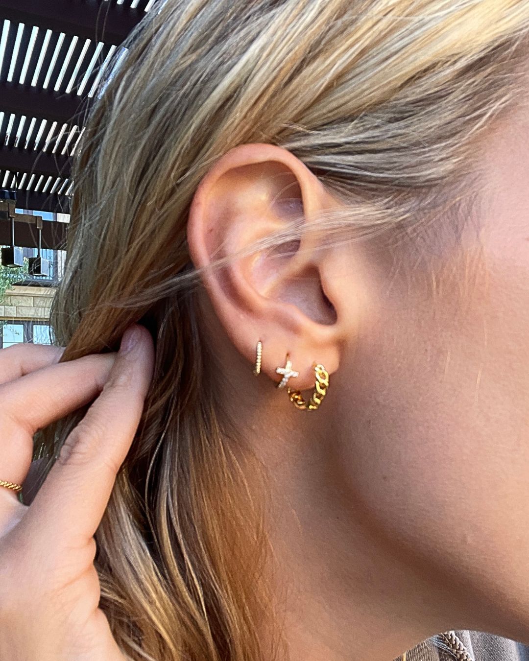 Ear worn with a crystal-set huggie, a small crystal cross stud and a gold chain-link hoop in stacked lobe piercings