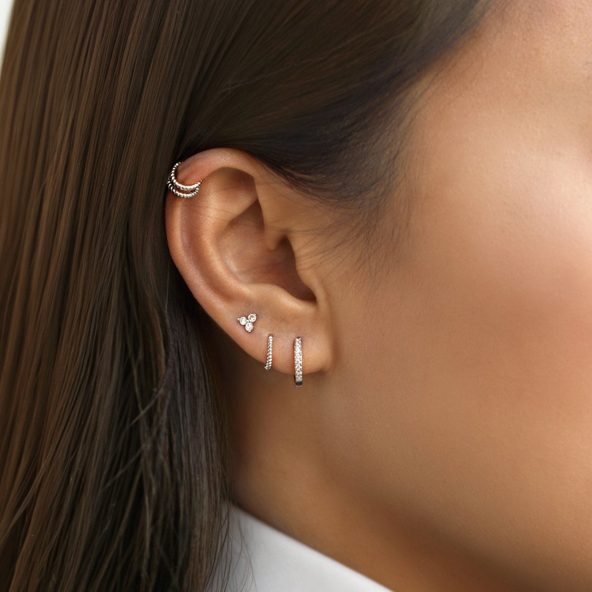 Sterling silver trio zirconia stud and pavé huggies shown on a model's ear with a cuff