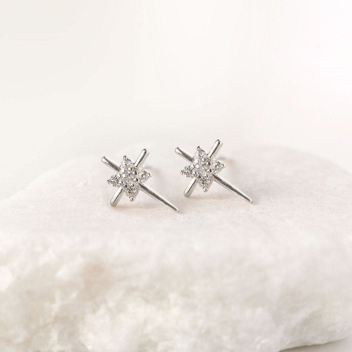 14K white gold thin cross stud earrings with clear zirconia stones, shown on a white stone