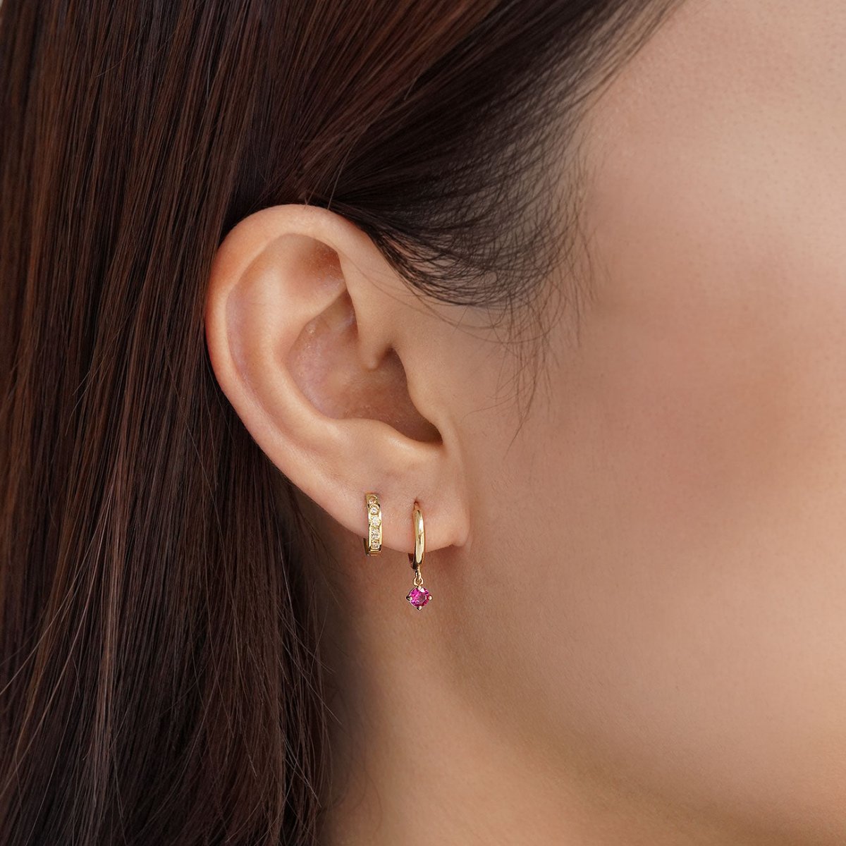 Close-up of woman's ear featuring 14K Gold Gemstone Dangle Huggies Ruby CZ Crystal paired with 14K Pave Huggie Earring
