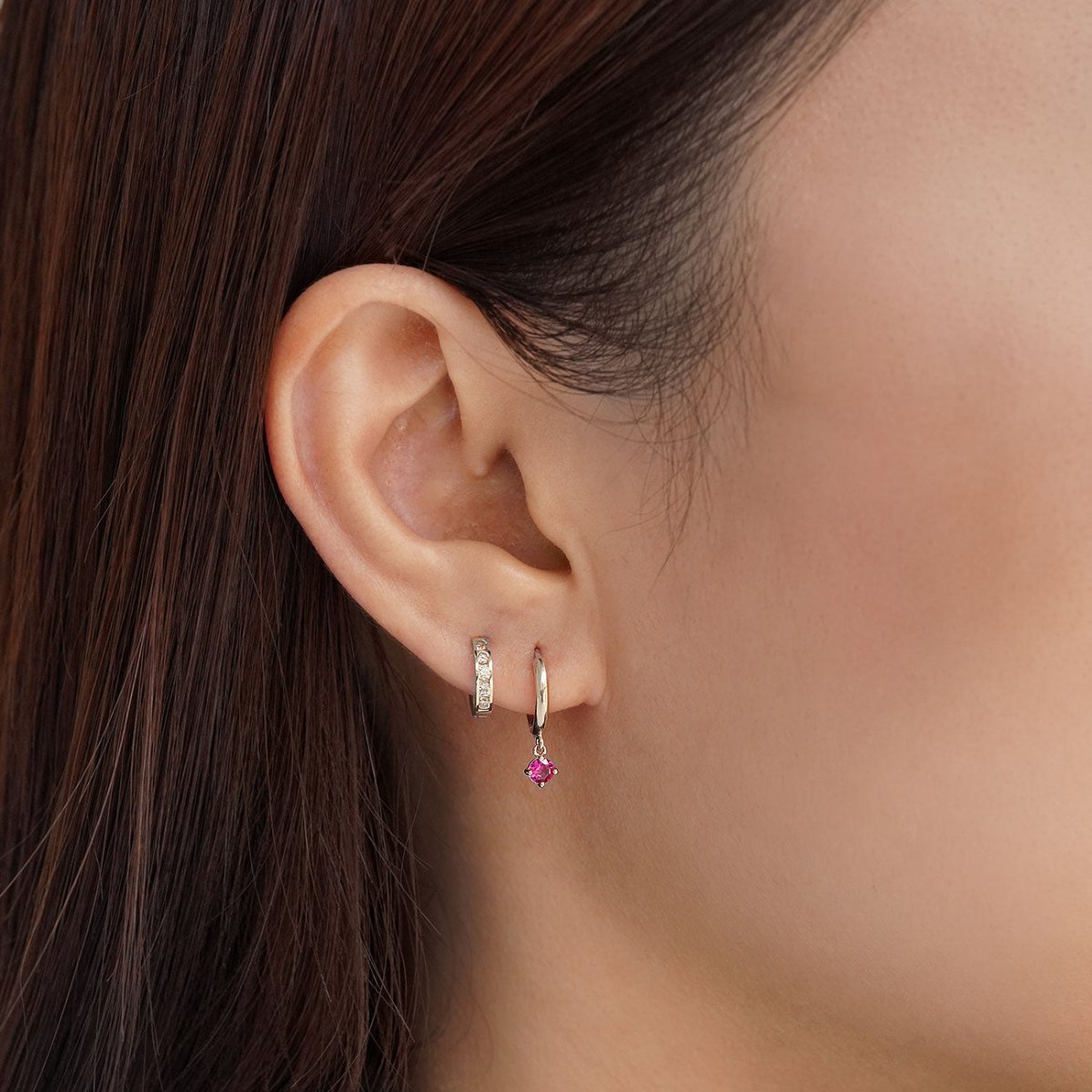 14K white gold ruby drop huggie hoop shown on a model's lobe in an ear stack