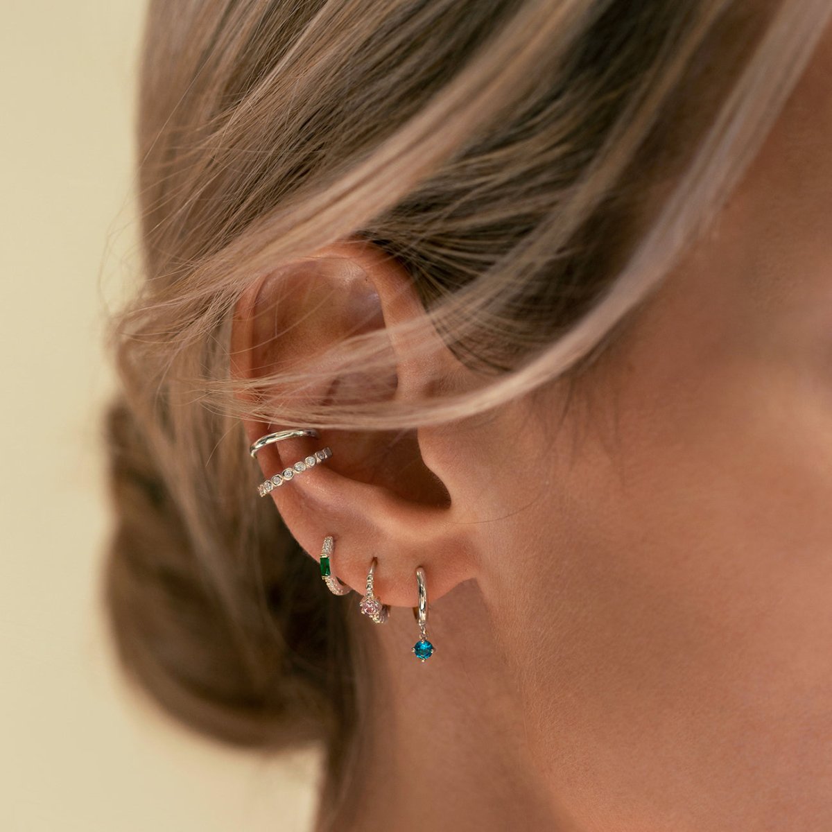 Sterling silver emerald baguette huggie hoop, shown on a model's ear stacked with other gemstone hoops