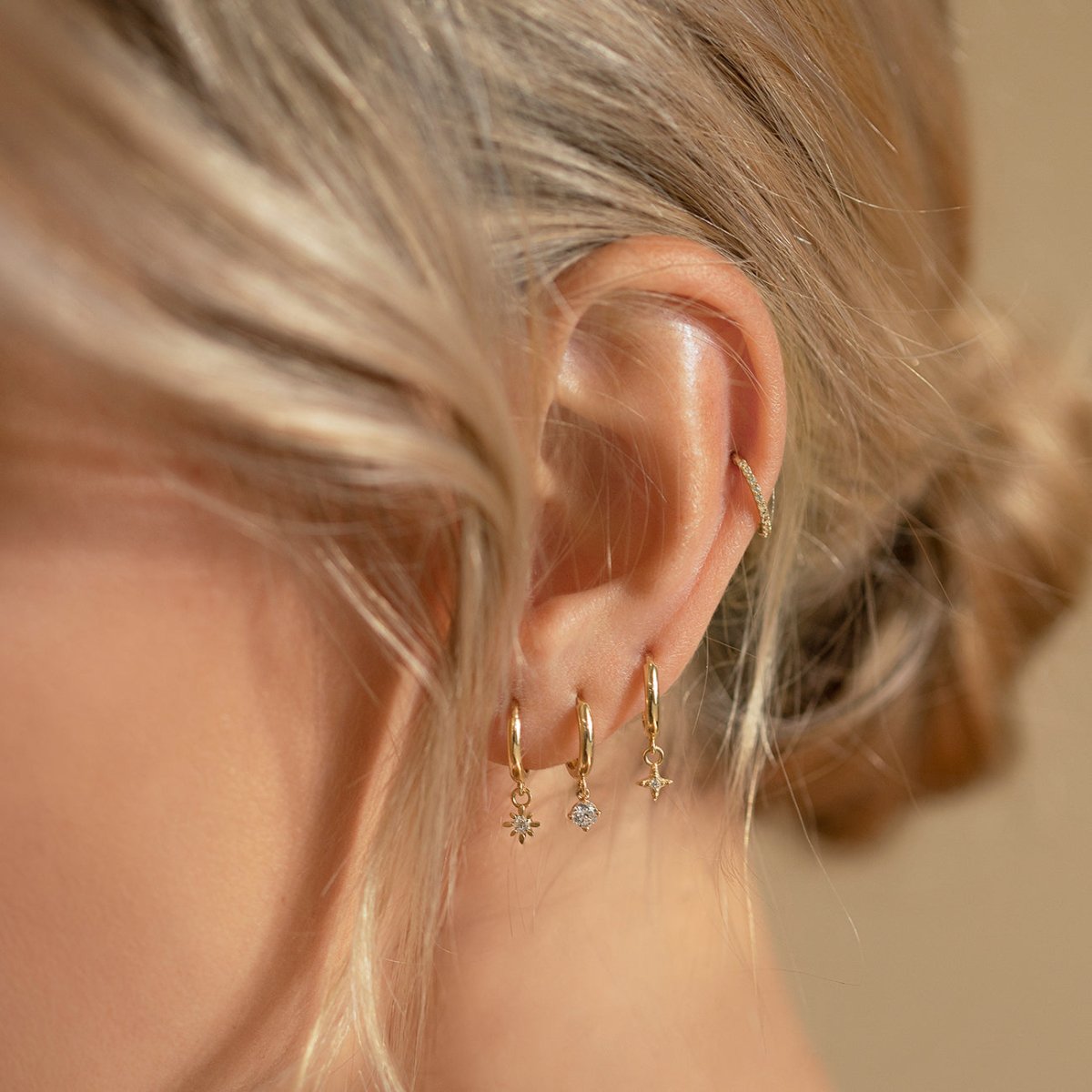 14K gold starburst-charm huggie hoops shown on a model's stacked lobe piercings