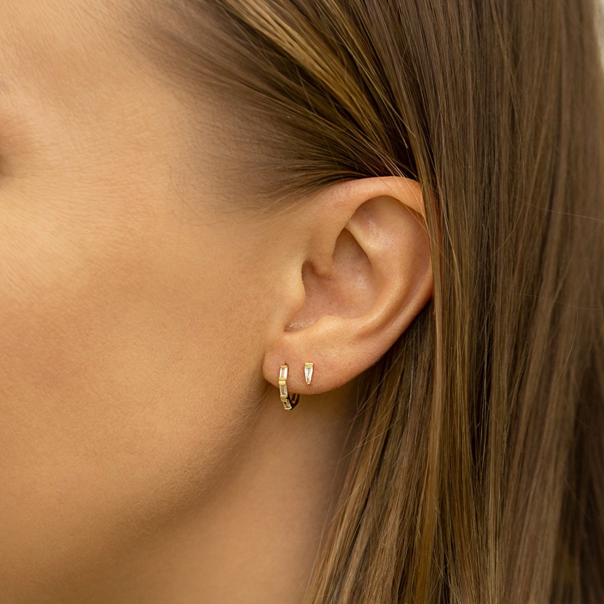 Gold vermeil tapered baguette stud with white zirconia, shown on a model's lobe beside a hoop
