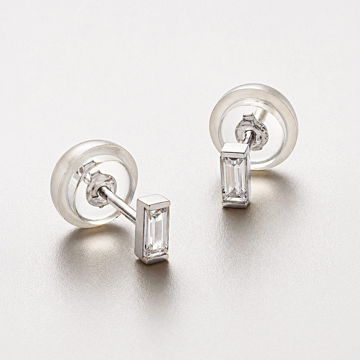 Pair of 14K white gold baguette studs with clear stones and silicone backs, on a light gray surface