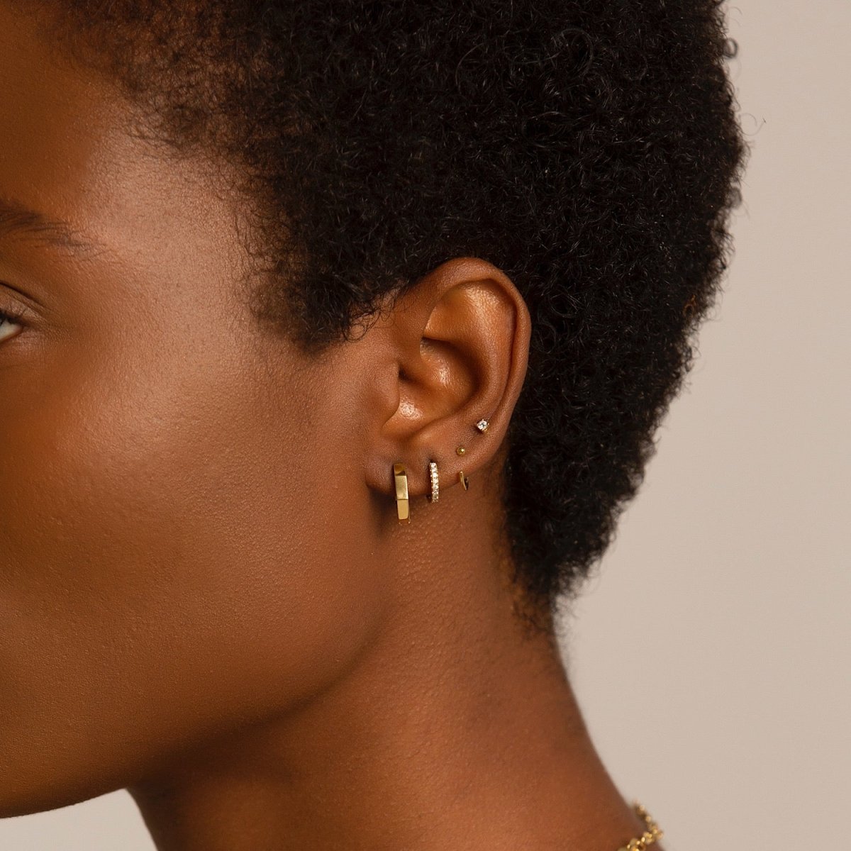 Gold vermeil huggie hoops shown stacked on a model's lobe and upper-lobe piercings