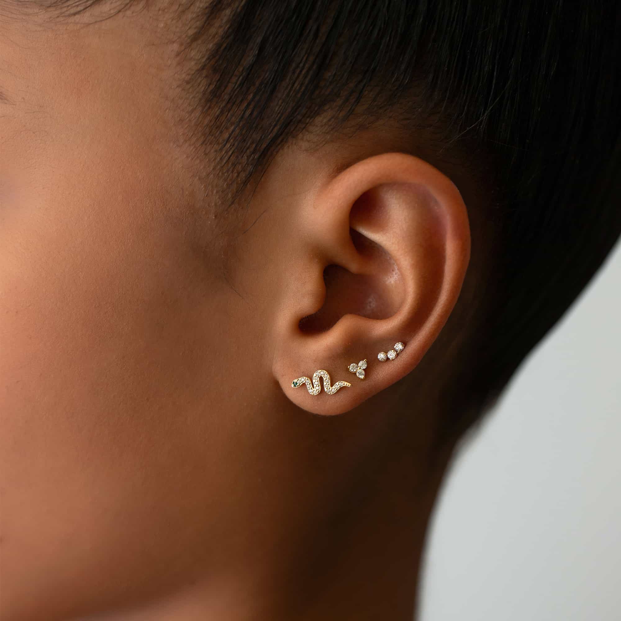 14K gold pavé snake stud shown on a model's ear with clear-stone cluster studs
