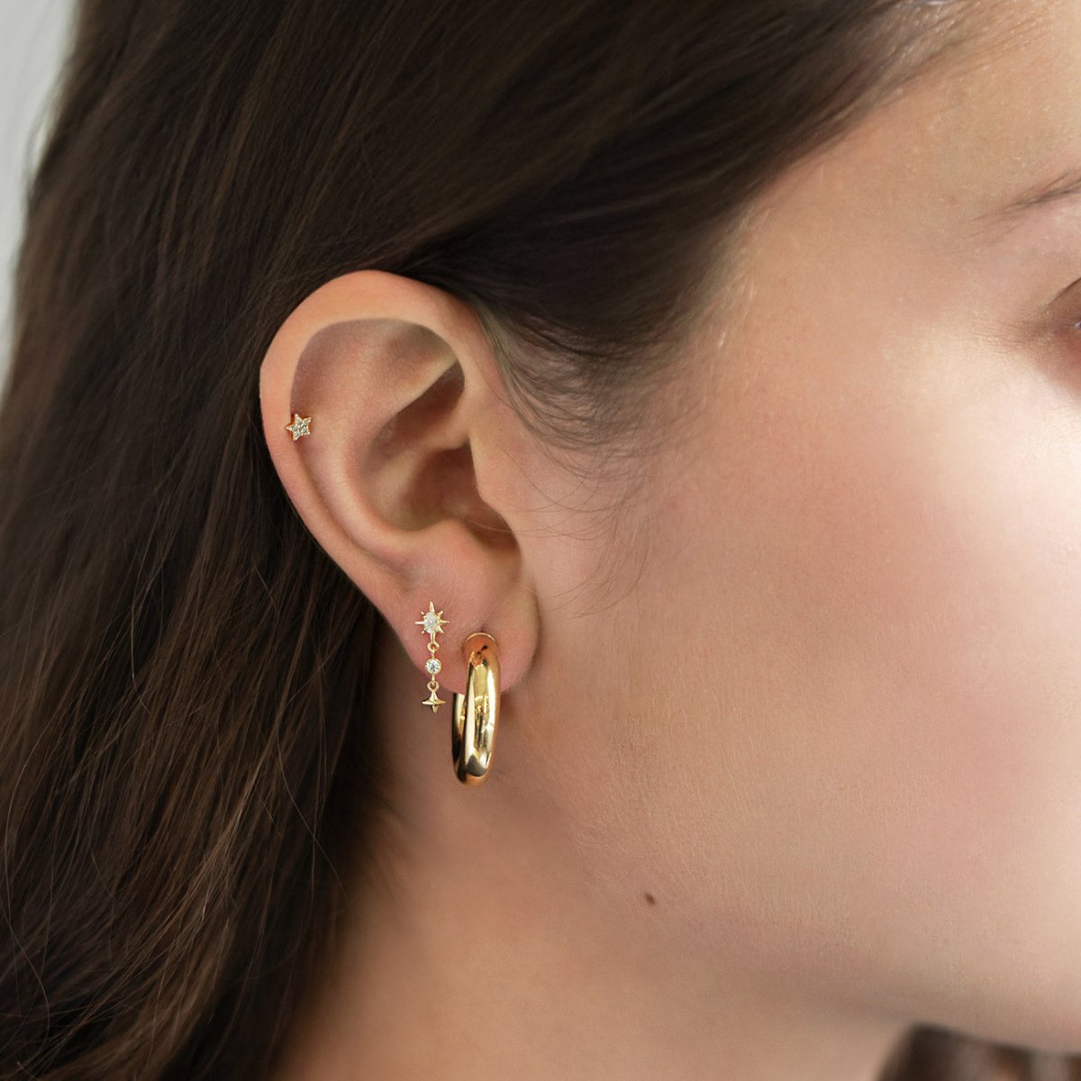 14K gold starburst drop earring with clear stones and hoop, shown on a model's lobe in an ear stack