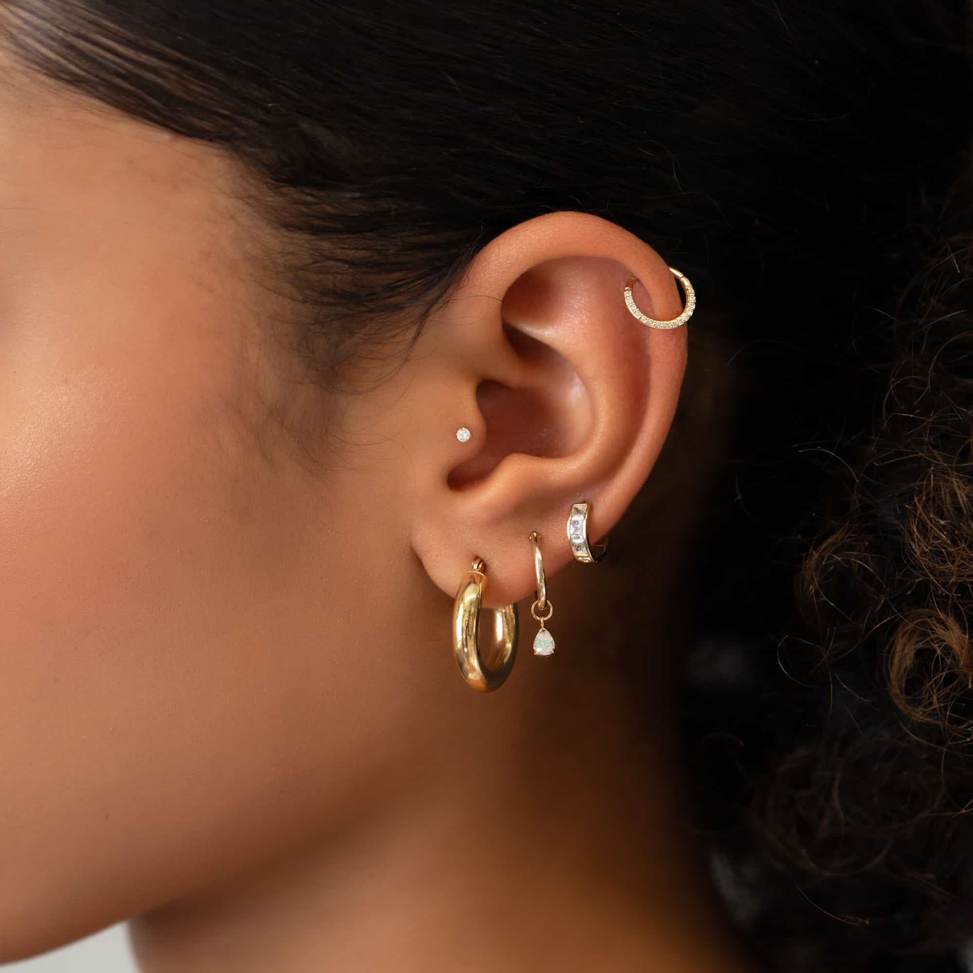Gold huggie hoop with a dangling white opal pear drop, shown in a stacked ear