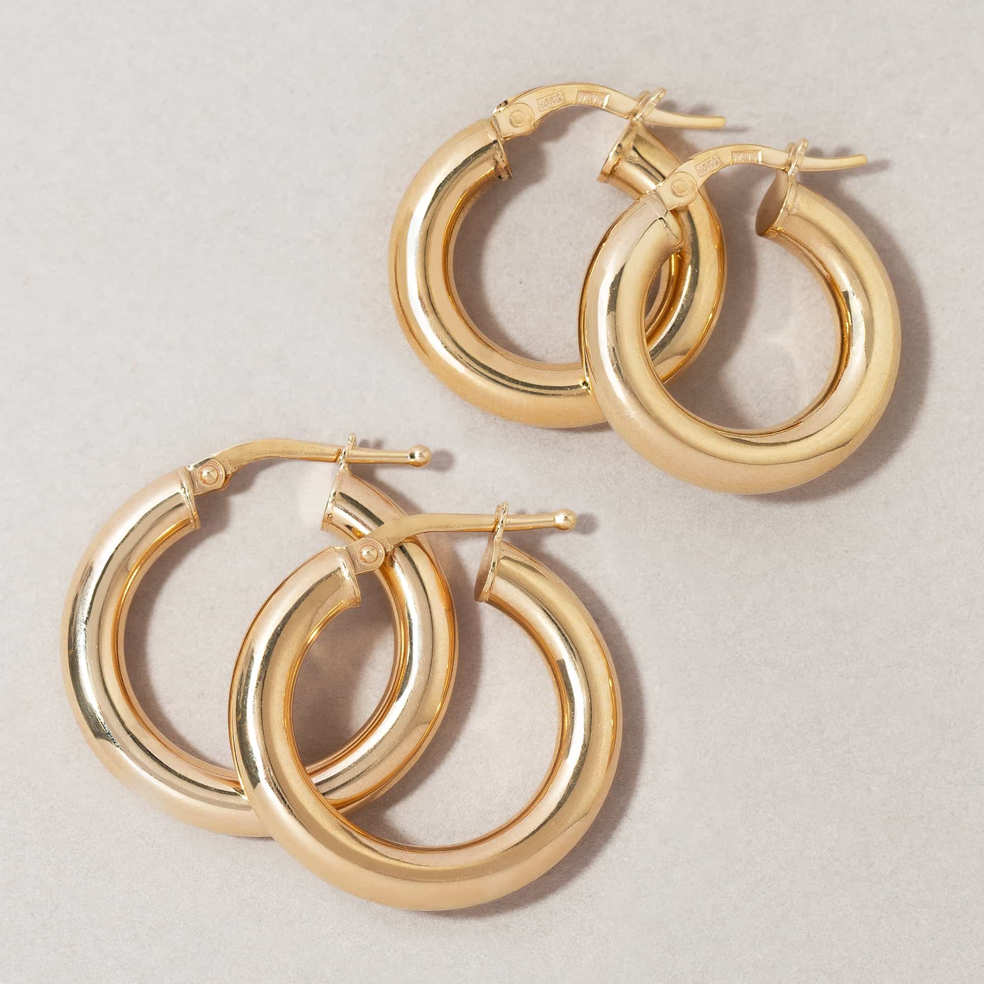 14K gold thick chunky latch-back hoop earrings in two sizes, on a cream surface