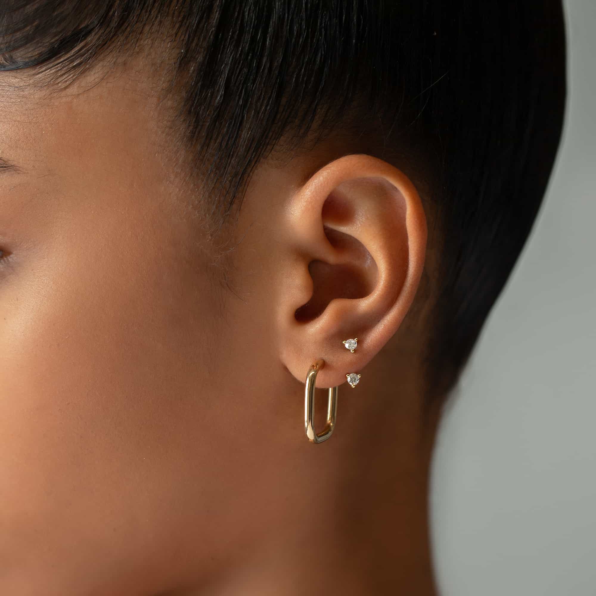 14K gold elongated oval hoop shown on a model's lobe with round studs above