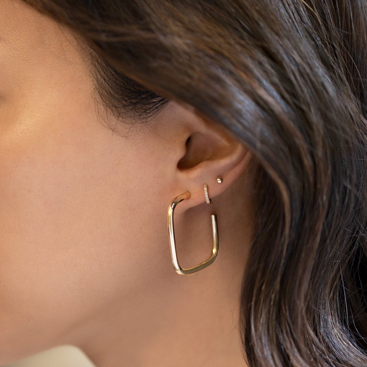 14K gold elongated square hoop shown on a model's lobe with small studs above