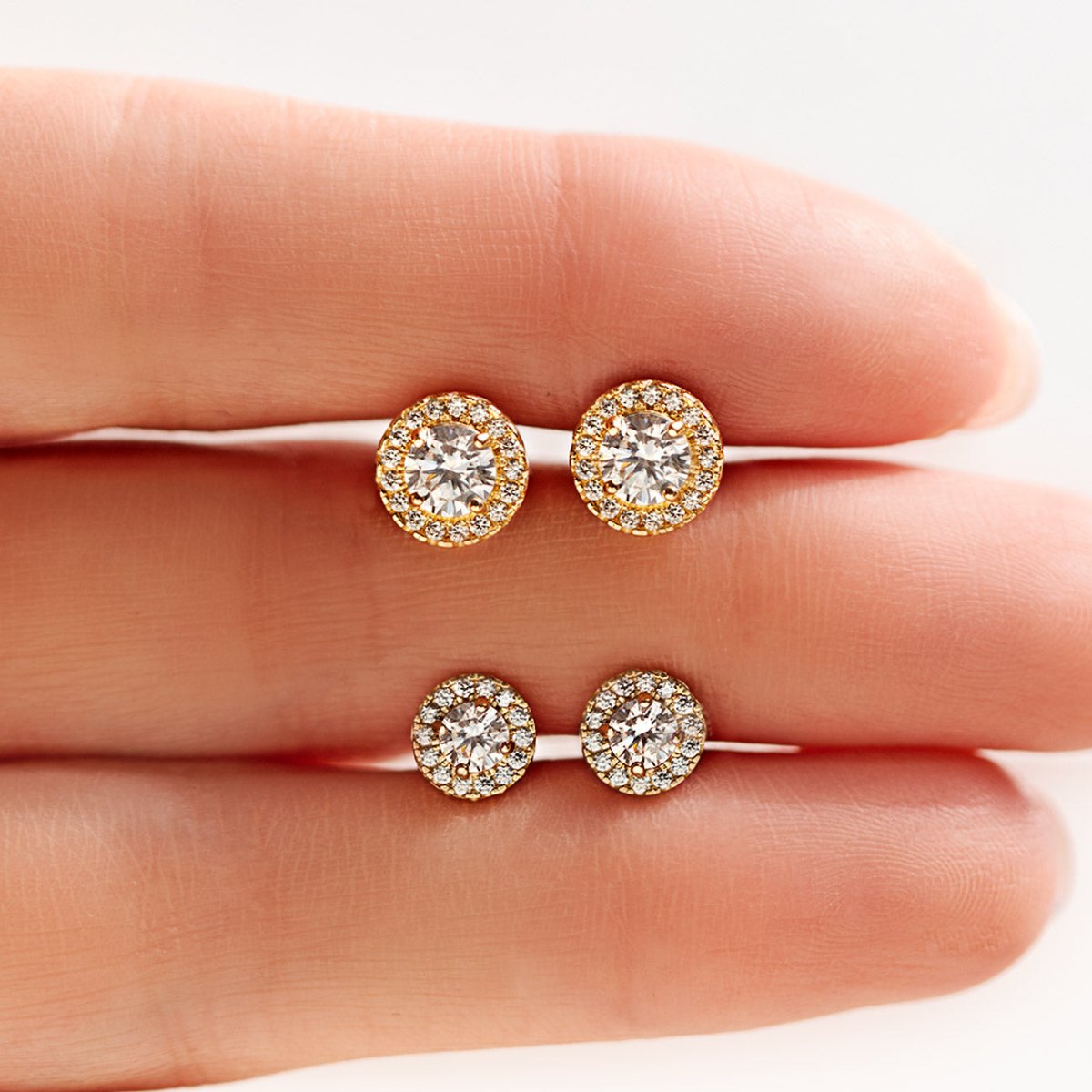 14K gold halo studs with clear stones in two sizes, held between fingertips | #Gemstone_White Zirconia