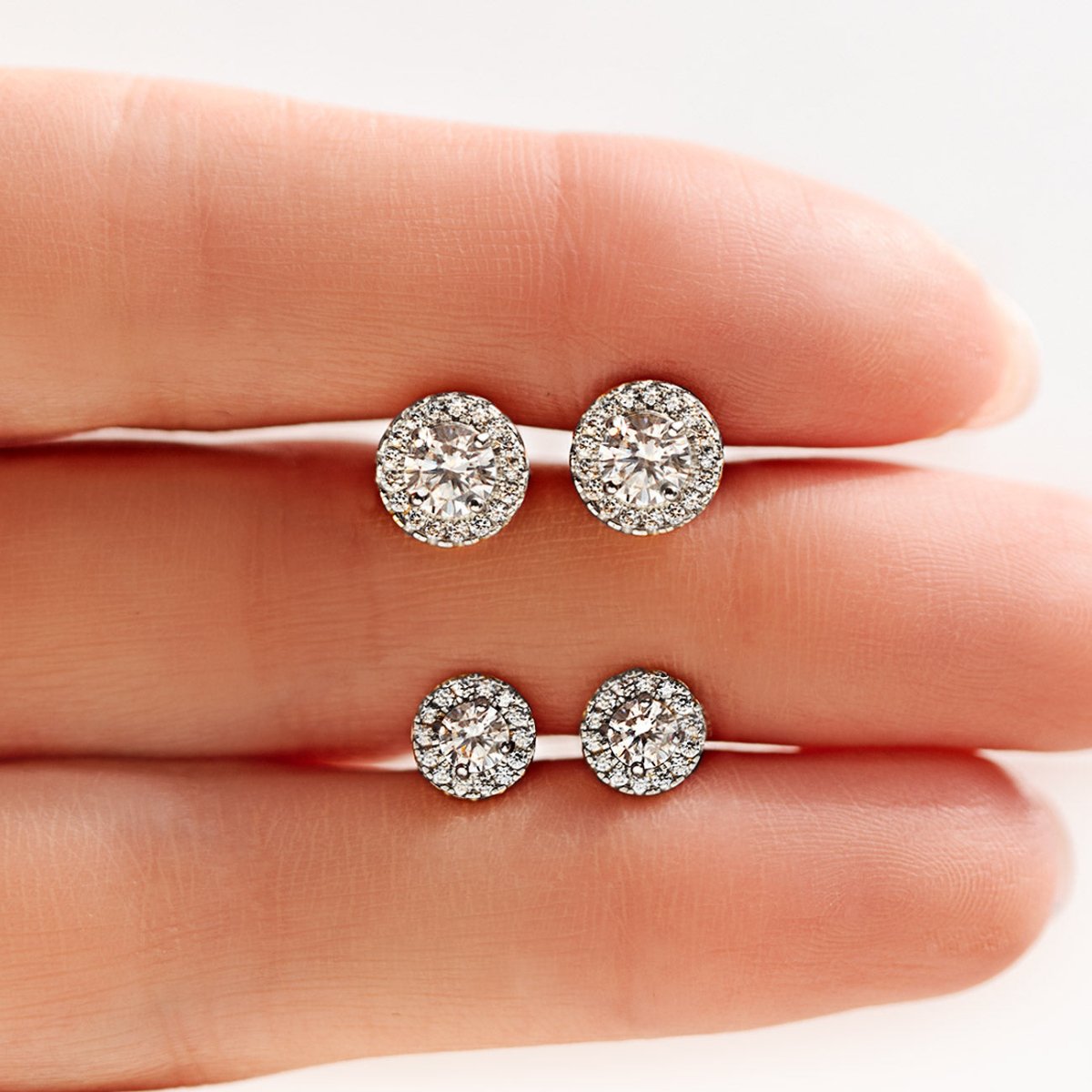 14K white gold halo studs with clear stones in two sizes, held between fingertips