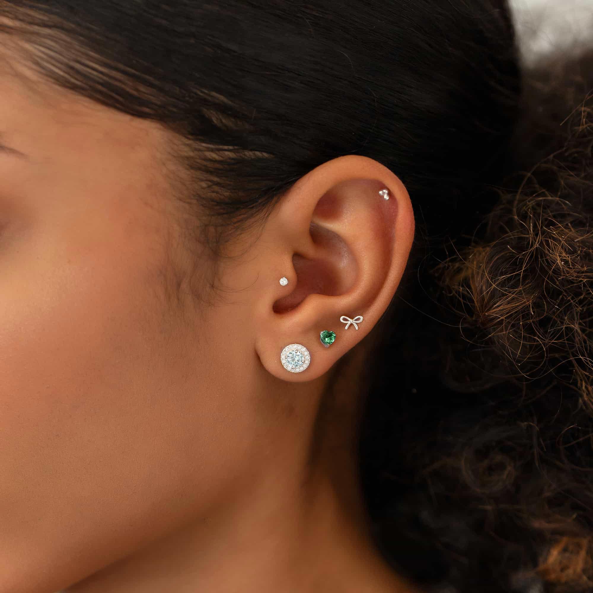 Close up of woman's ear featuring 14K White Gold Tiny Bow Single Stud and other gemstone stud earrings 