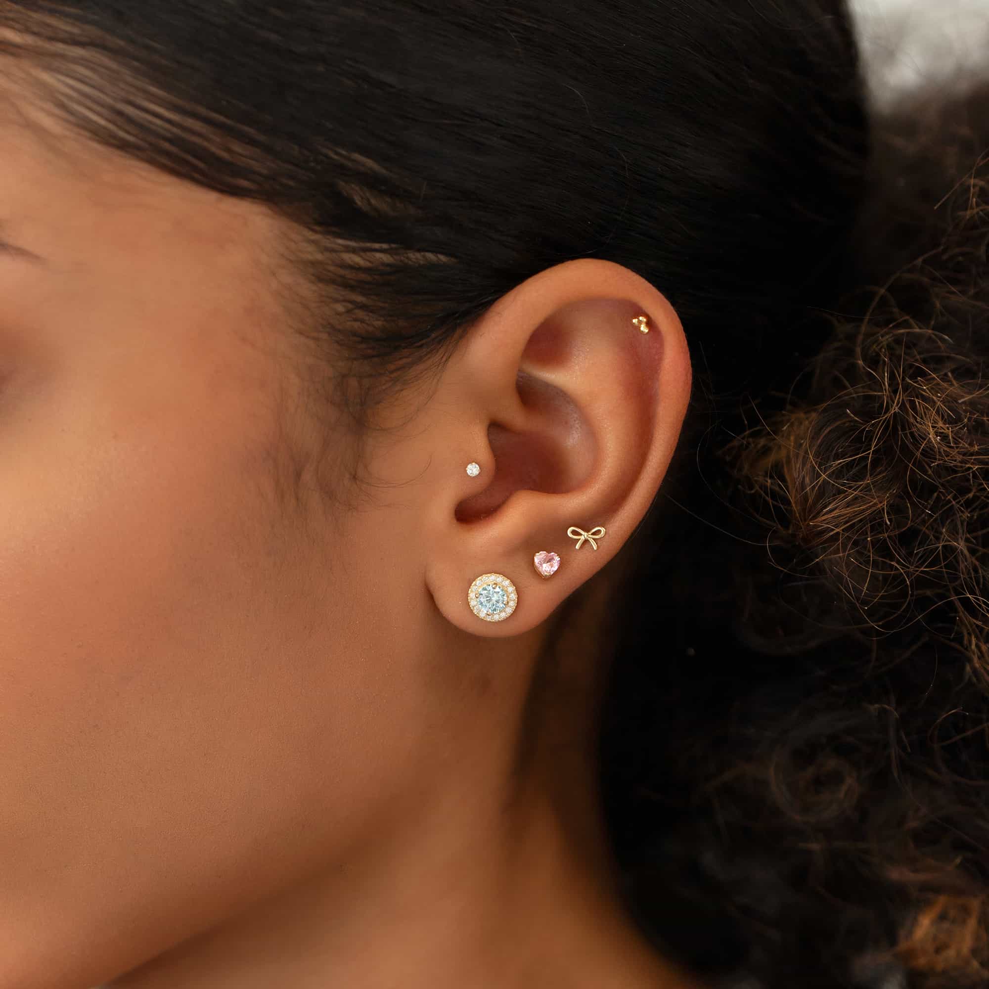 Close up of woman's ear featuring 14K Gold Tiny Bow Single Stud and gemstone earrings 