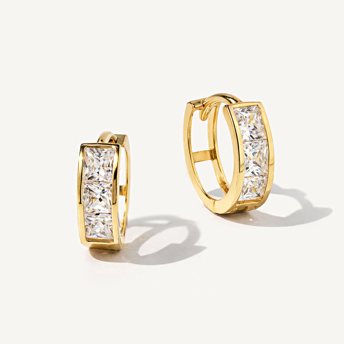 14K gold princess-cut huggie hoops with clear white zirconia, shown front and side on a cream background