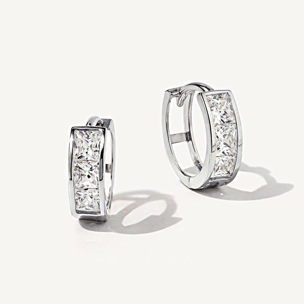14K white gold princess-cut huggie hoops with clear white zirconia, close-up detail on a cream background