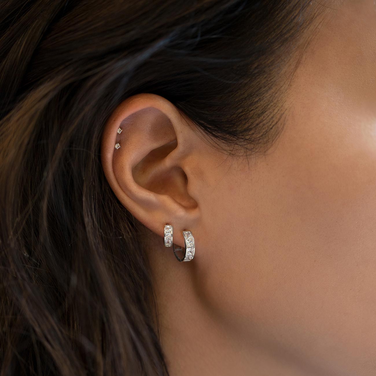 Sterling silver flat back stud with clear zirconia stones, shown as huggie hoops on a model's lobe