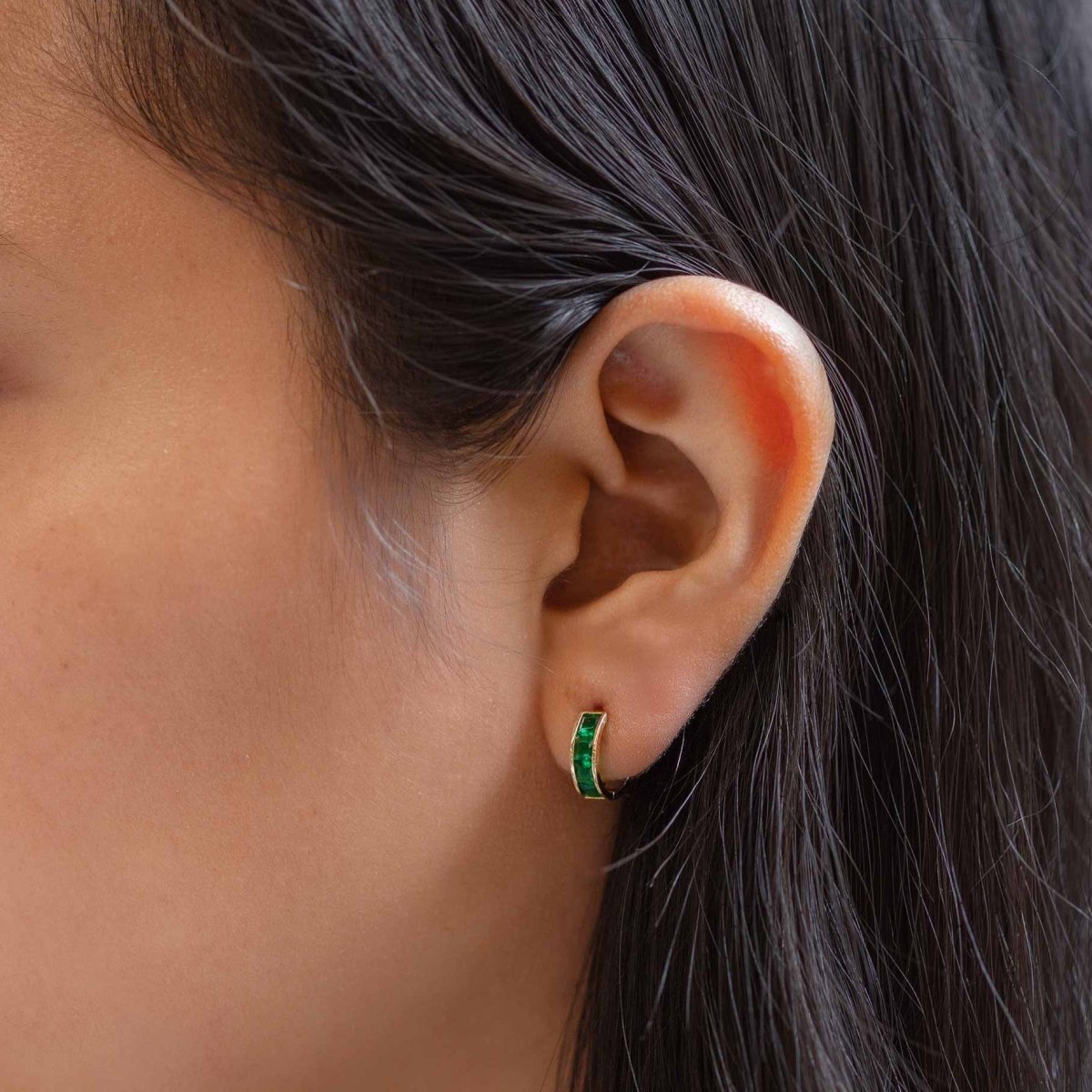 14K gold emerald huggie hoop with square green stones, shown on a model's lobe