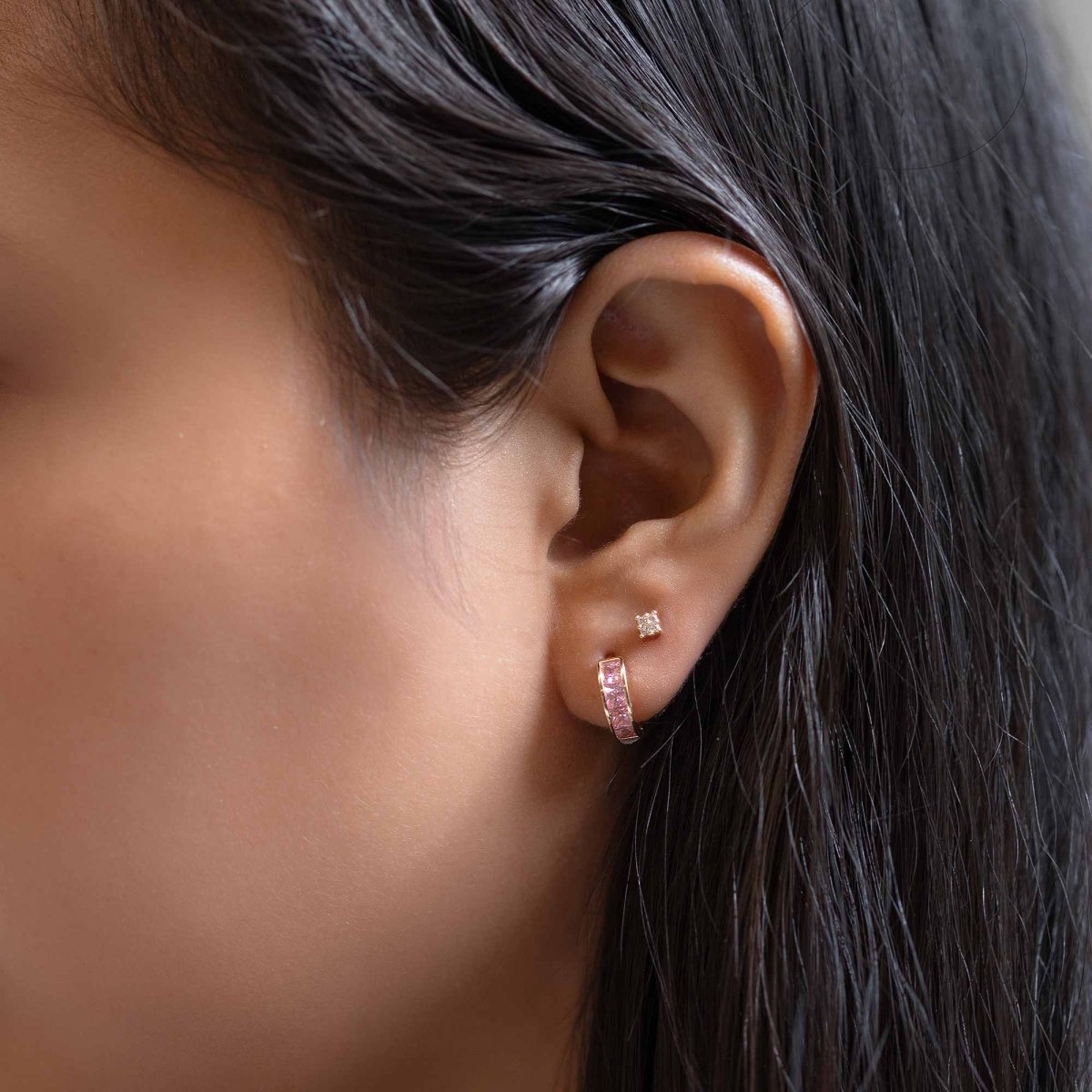 Rose-tone huggie and clear stud shown on a model's lobe and second piercing