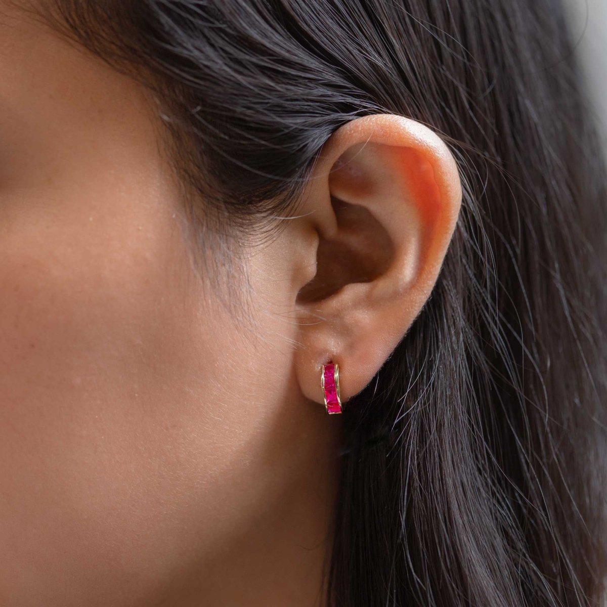 14K gold ruby huggie hoop with square red stones, shown on a model's lobe