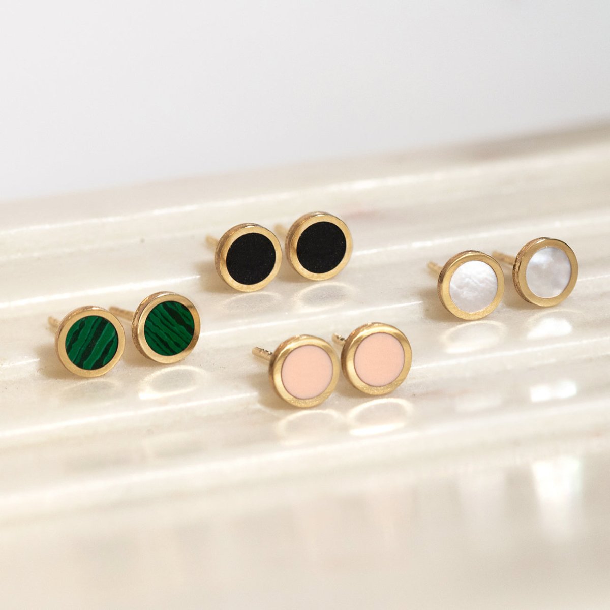14K gold round bezel rose quartz studs shown with other color inlays on a ridged surface