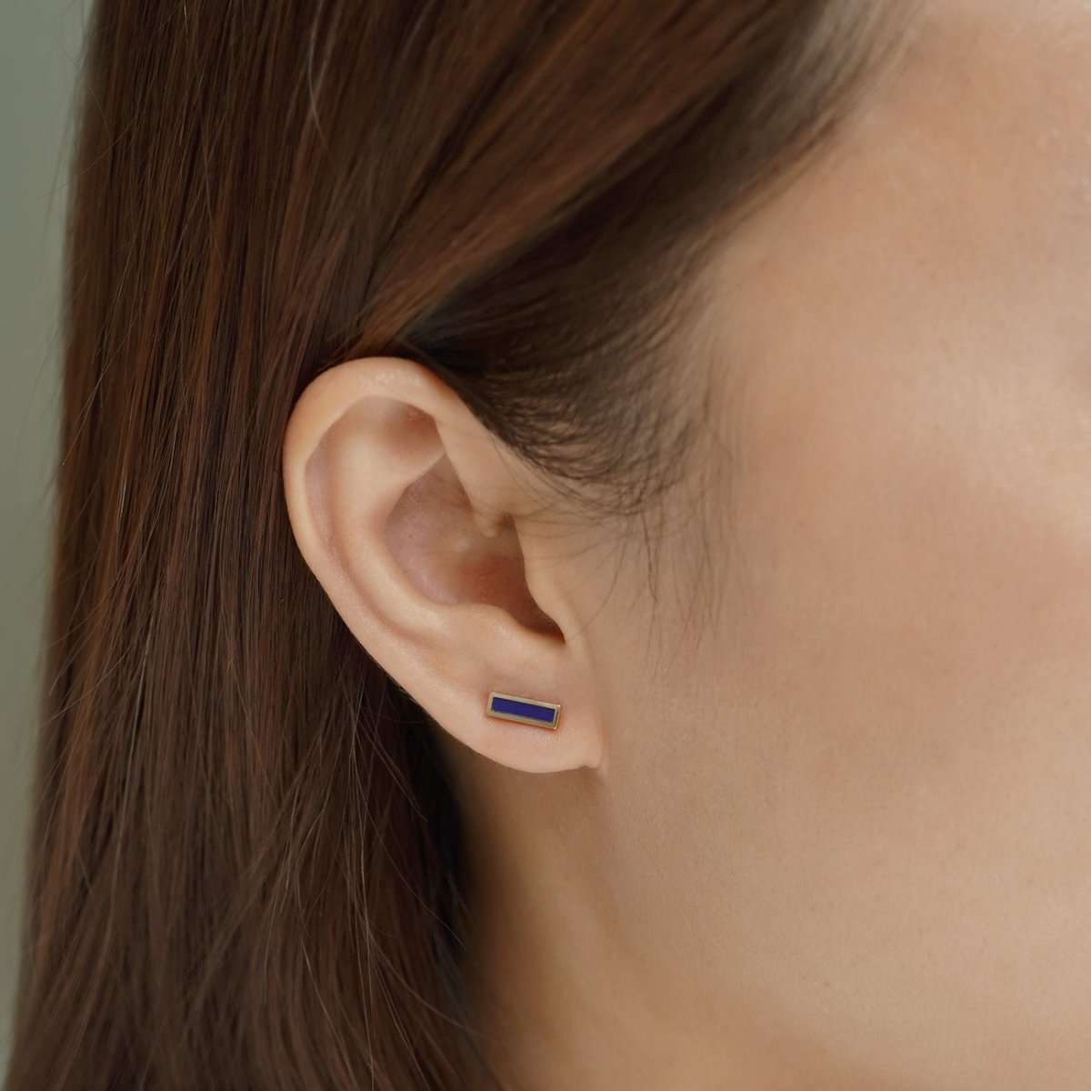 14K gold lapis lazuli bar stud with a blue rectangular stone, close-up on a model's lobe
