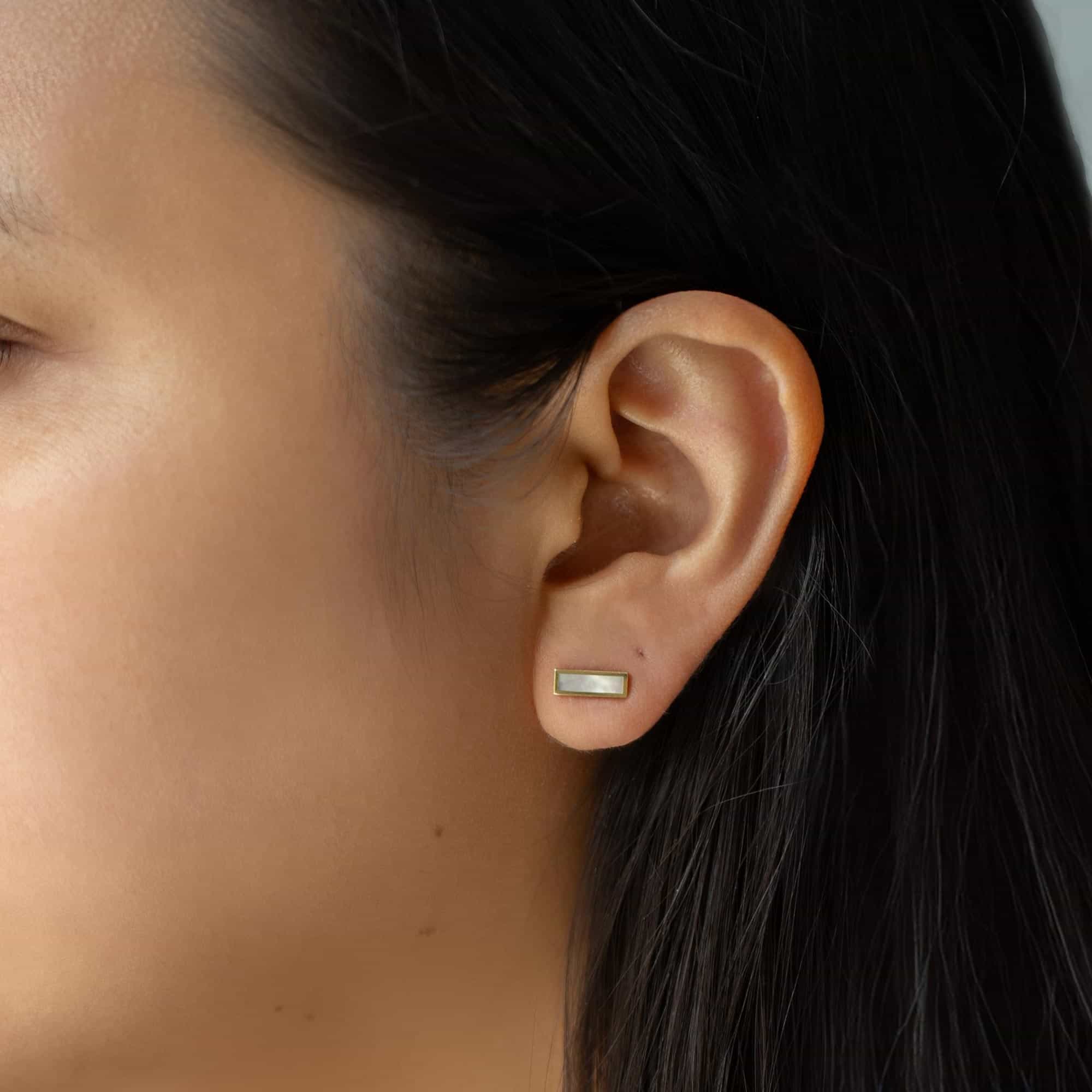 14K gold mother of pearl bar stud with a white iridescent stone, close-up on a model's lobe