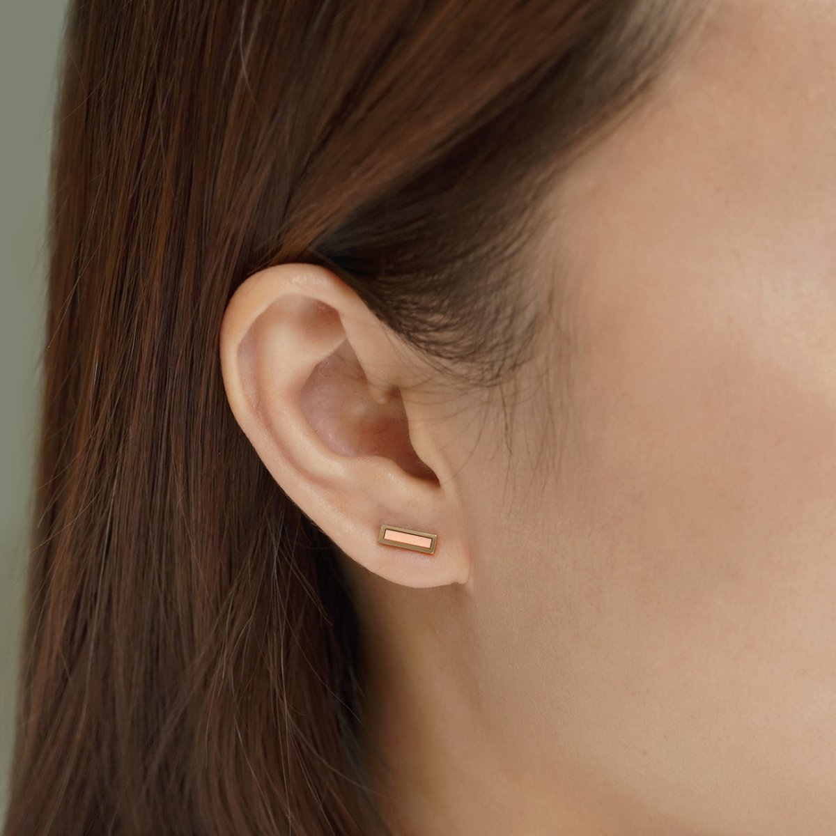 14K gold rectangular bar stud with a pink inlay, shown on a model's earlobe