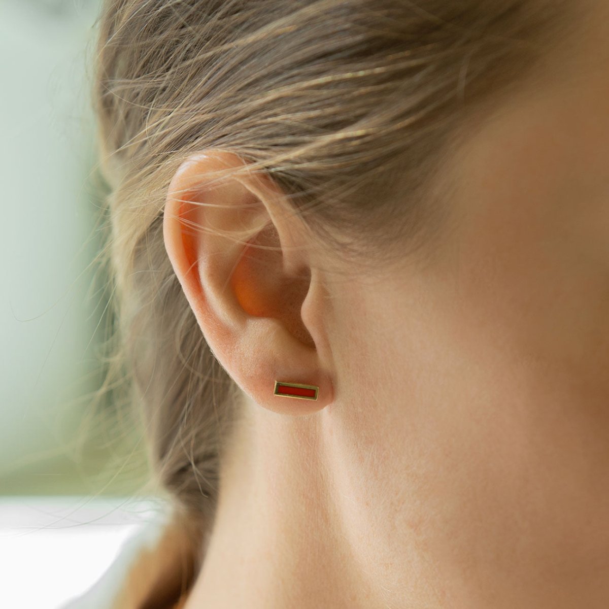 14K gold carnelian bar stud with a red rectangular stone, shown on a model's lobe