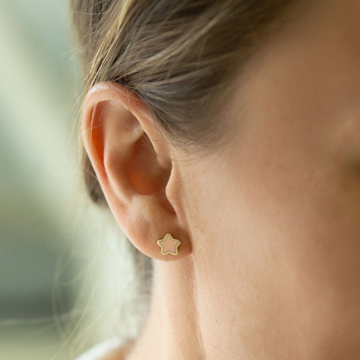 14K gold rose quartz star stud shown close on a model's earlobe