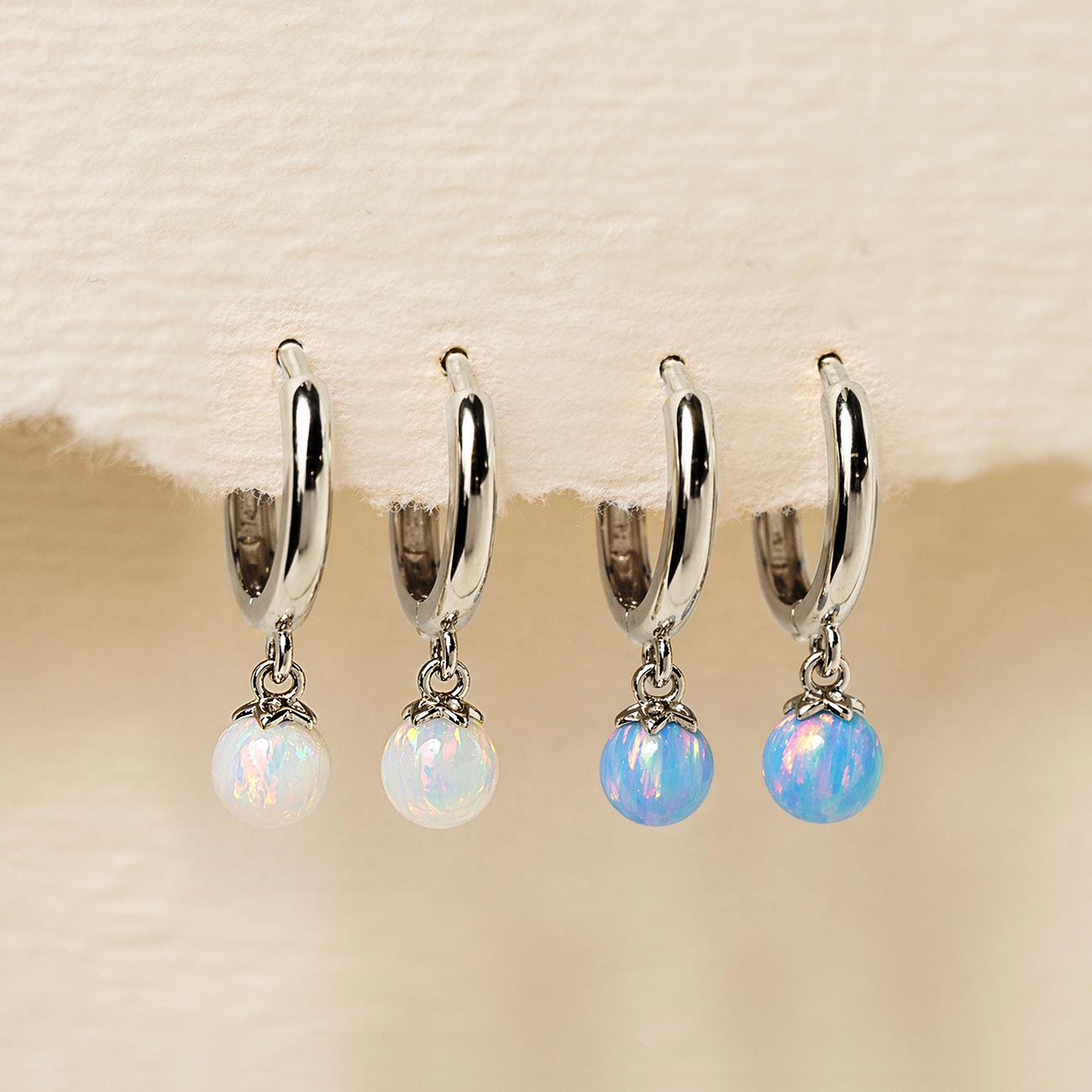 14K white gold opal huggie hoops shown in white and light blue opal beads, on a cream background