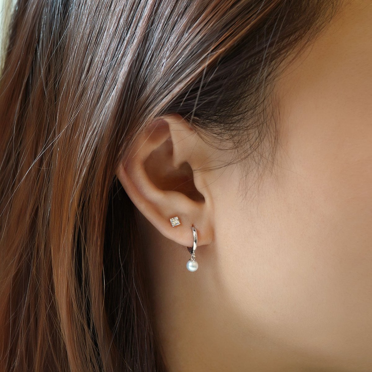 14K white gold huggie hoop with a small dangling pearl, shown on a model's lobe