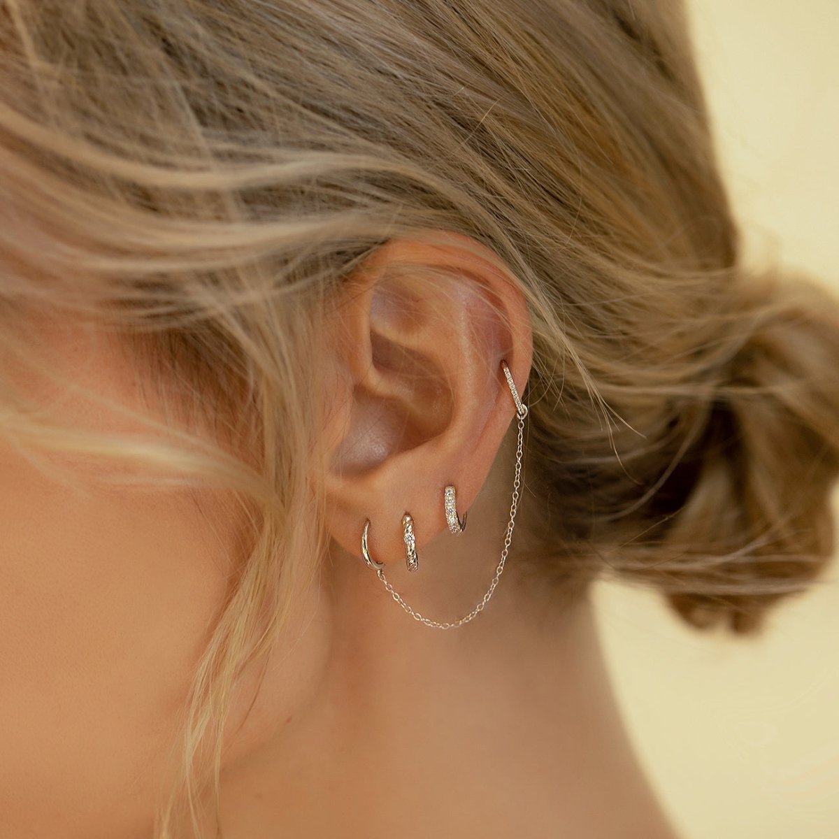 14K white gold rope twist huggie with clear stone in a hoop and chain ear stack on a model