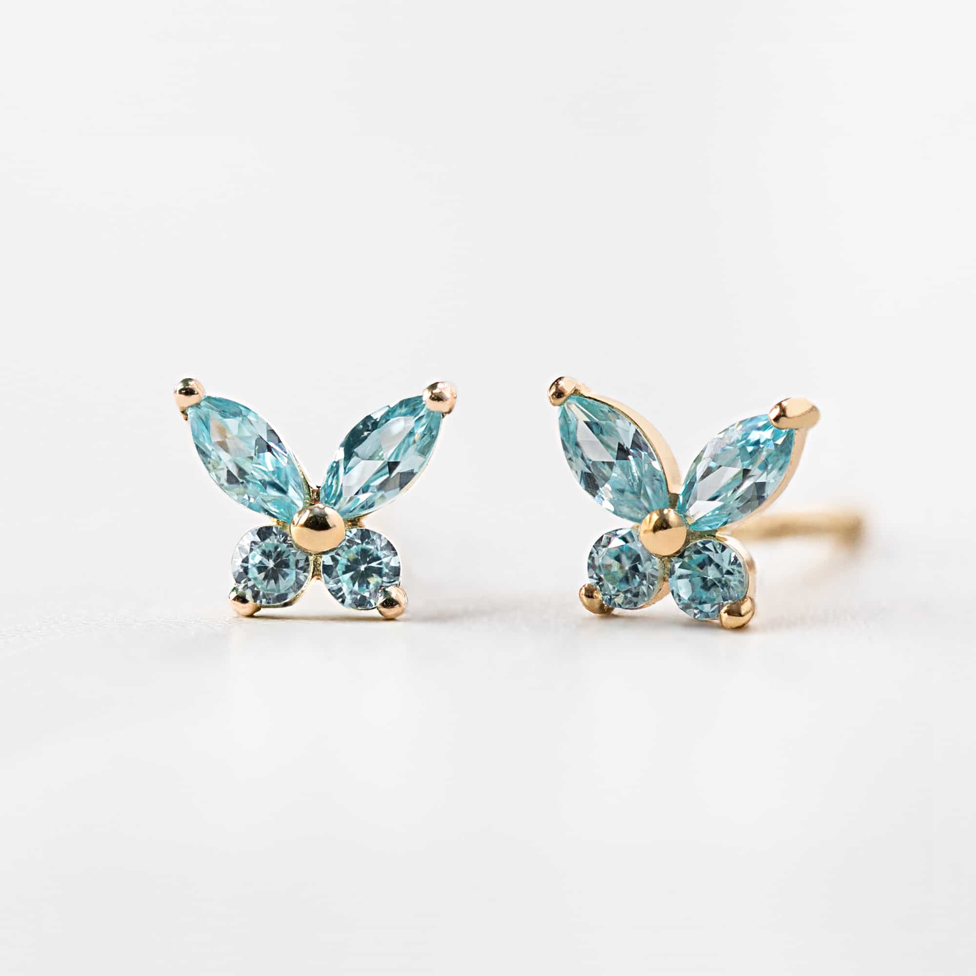 14K gold aquamarine butterfly studs with light blue stones, close-up detail on white marble