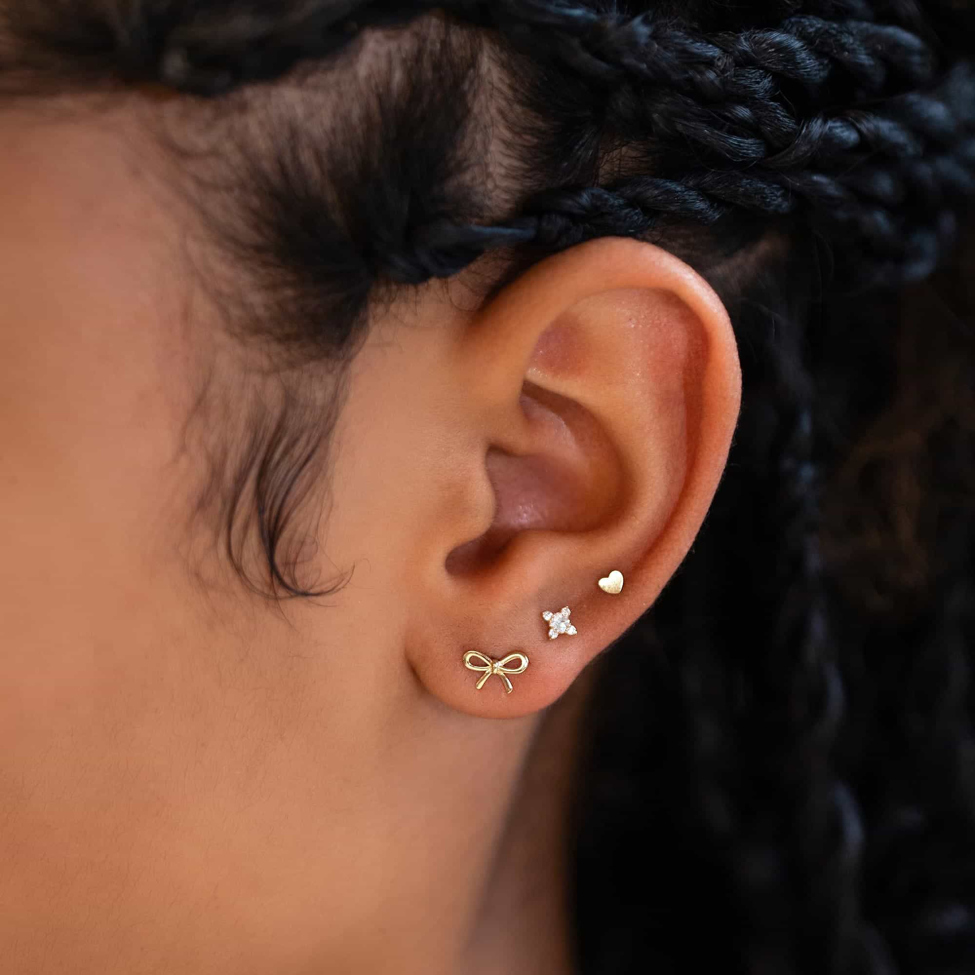 14K gold tiny heart stud shown in an upper-lobe ear stack on a model