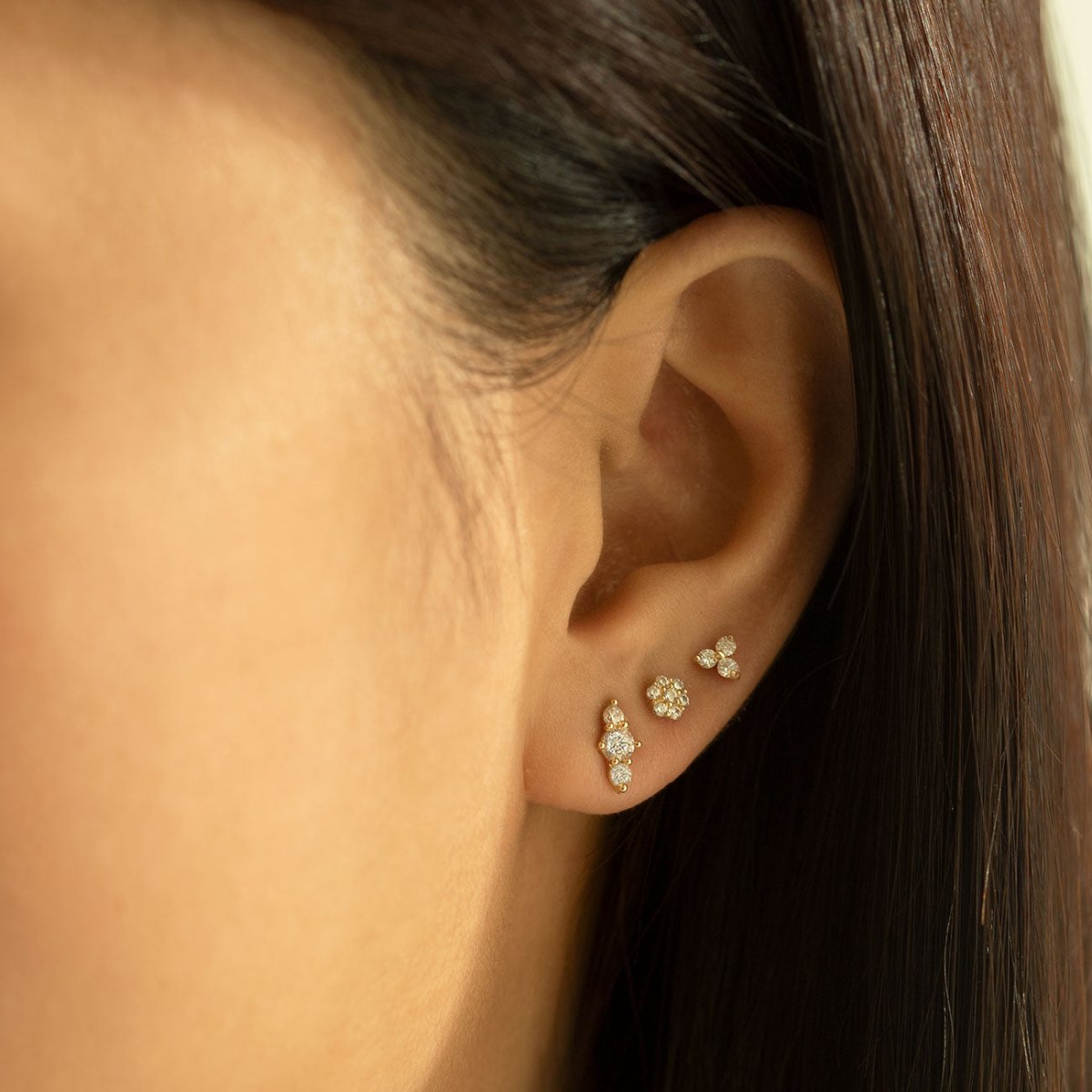Close up of woman's ear featuring 14K Solid Gold Trio Bar Pave Studs and other stud earrings 