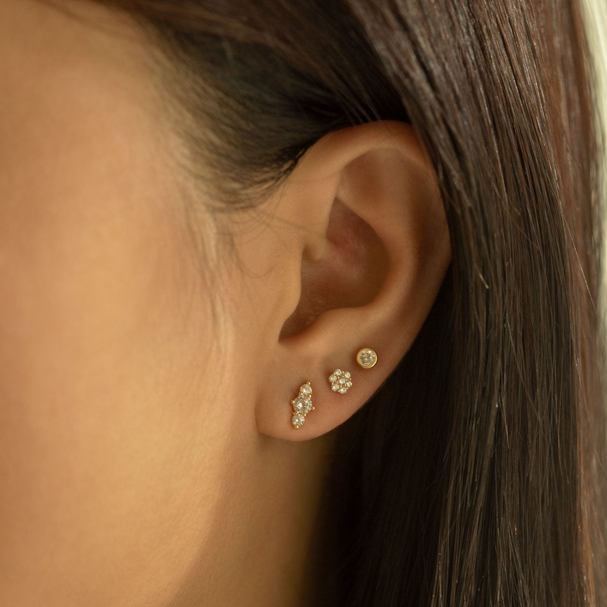 14K gold bezel zirconia stud worn on a model's lobe beside cluster studs in an ear stack