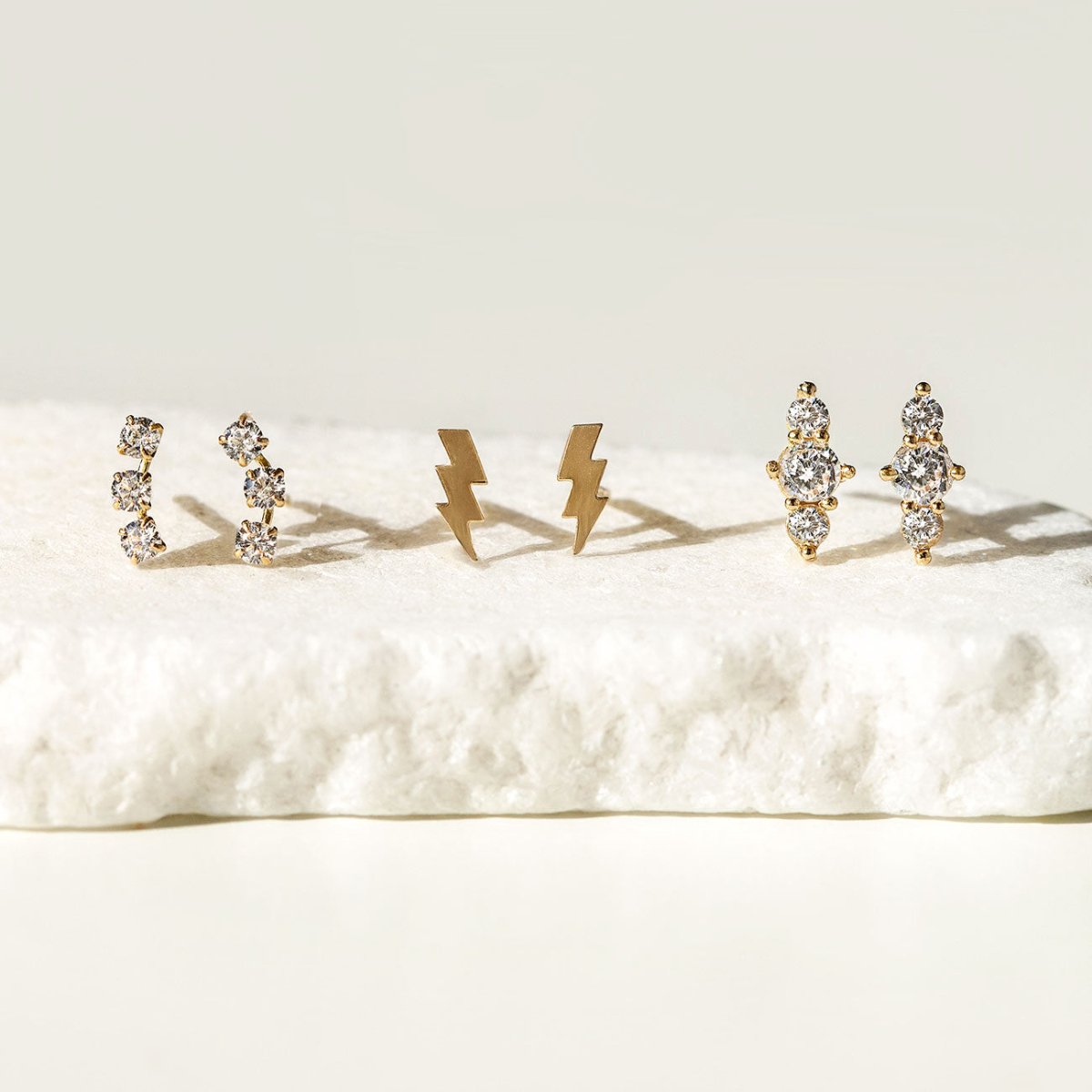 Close-up of 14K Solid Gold Curve Pave Bar Studs, 14K Solid Gold Trio Bar Pave Studs, 14K Gold Vermeil Tiny Lightning Bolt Studs 