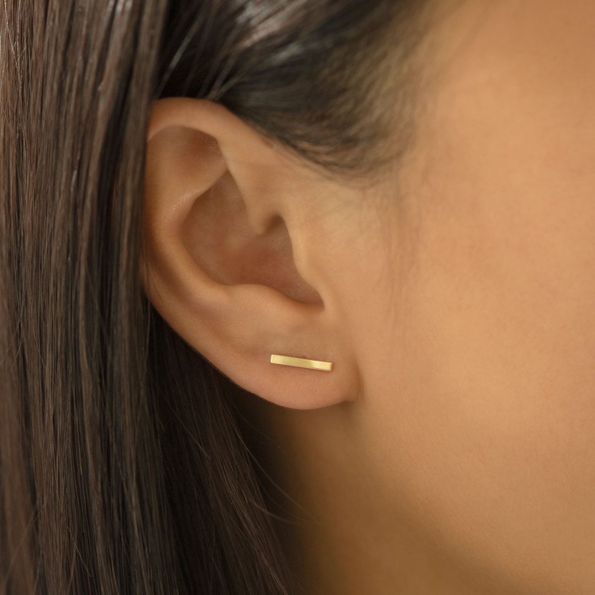 14K gold bar stud shown on a model's lobe, horizontal bar across the ear