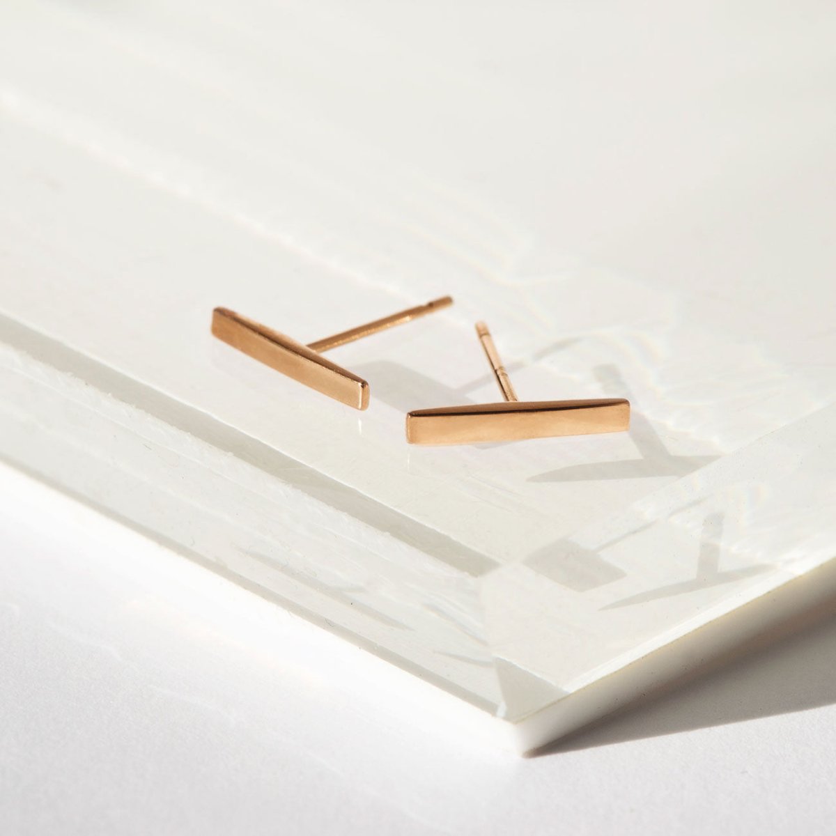 14K rose gold bar stud earrings angled on a white tray, posts visible