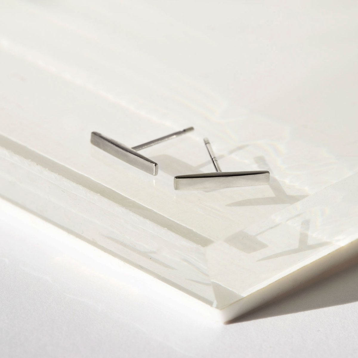 14K white gold bar stud earrings angled on a white tray, posts visible