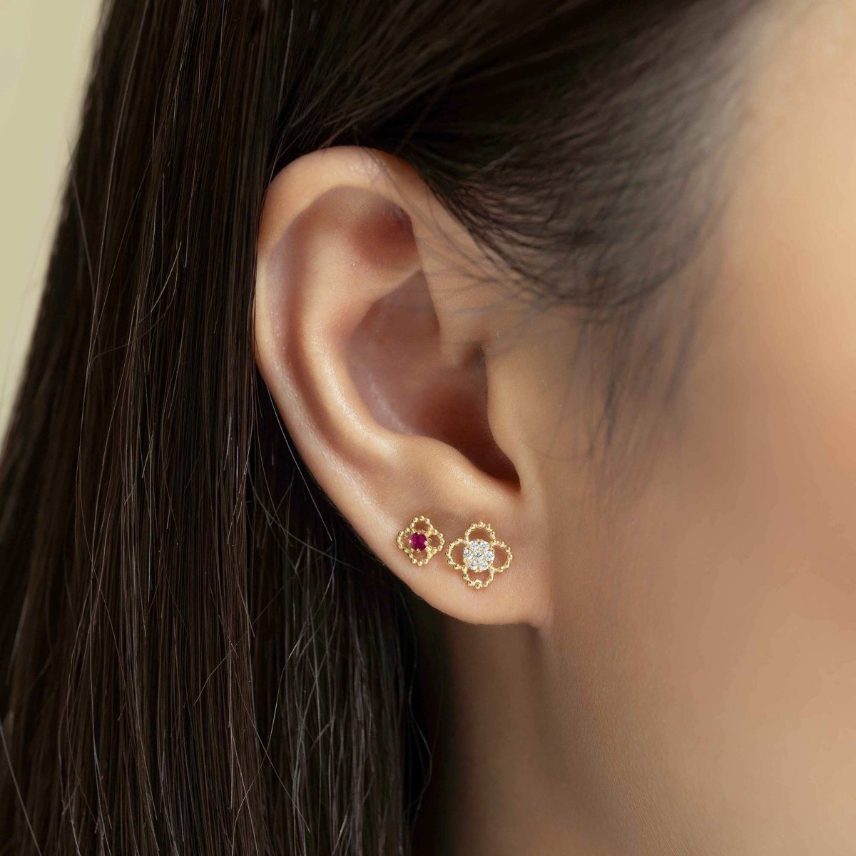 14K gold ruby flora stud worn beside a clear-stone flora stud on a model's lobe