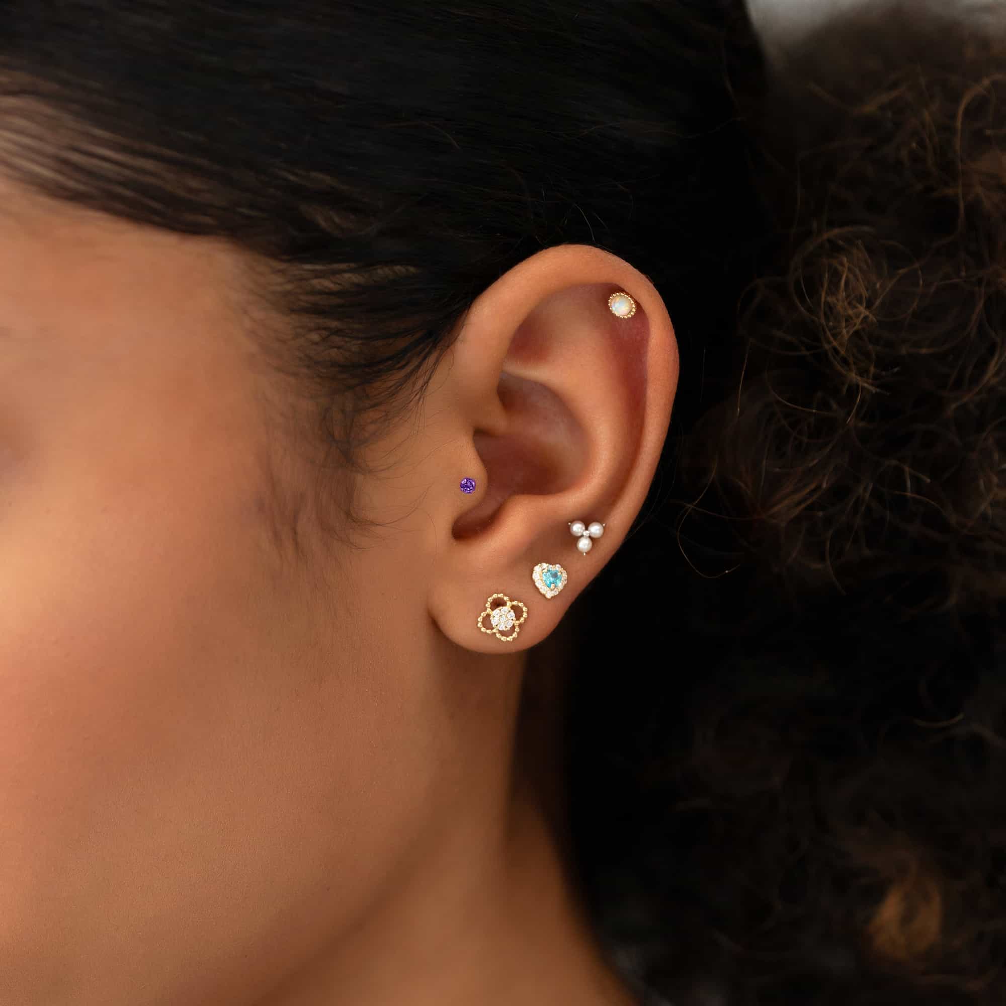 14K gold flat back amethyst stud shown on a model's lobe among colorful curated studs