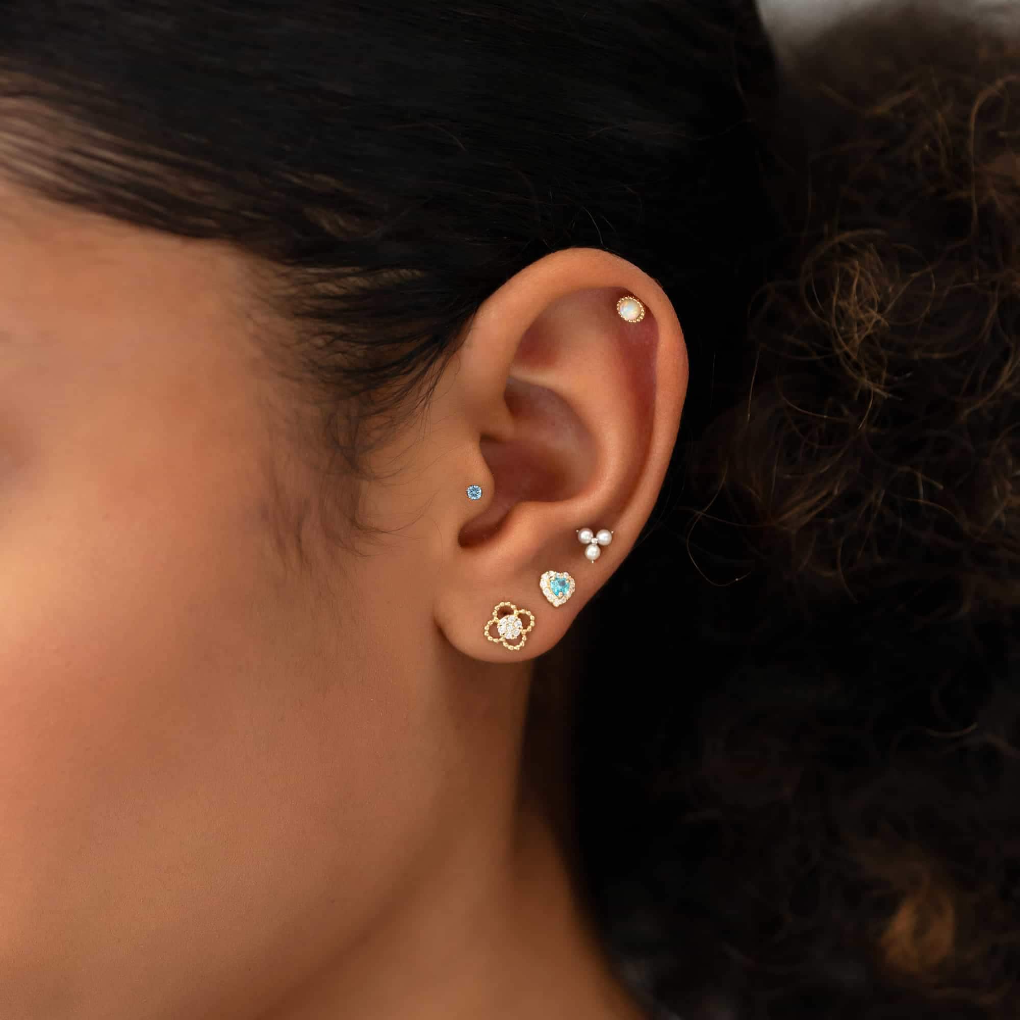 Gold studs including flower, heart and clear stone designs shown stacked on a model's ear