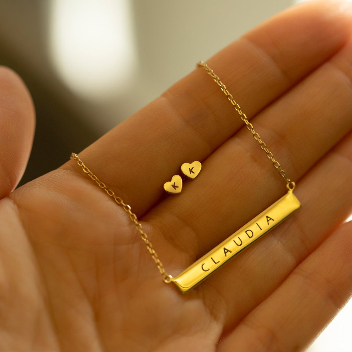 14K gold tiny heart initial studs shown beside a personalized gold bar name necklace